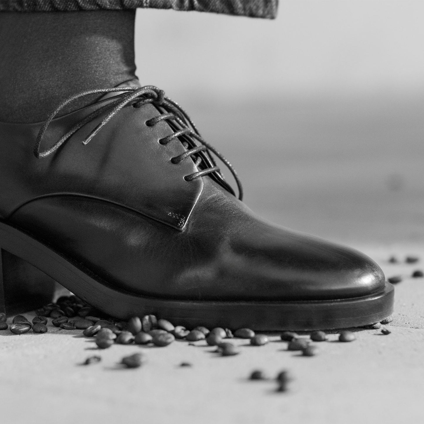 Black leather shoe with laces on a surface with coffee beans